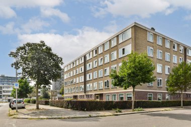 Geniş pencereleri ve yeşillikleri olan, bulutlu bir gökyüzüne karşı kurulmuş modern bir yerleşim yeri. Temiz tasarım şehir manzarasını geliştirir..