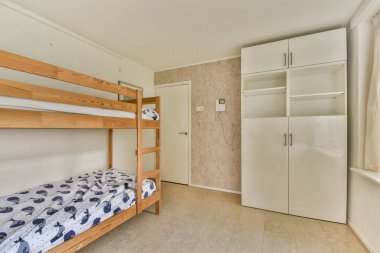 Güzel tasarlanmış minimalist bir yatak odası ahşap bir ranza ve parlak beyaz bir gardırop, rahat ve işlevsel bir yer yaratıyor..