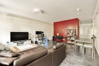 Koyu renkli bir kanepe, televizyon ve kırmızı aksanlı bir duvarın olduğu şık bir oturma odası. Uzay, çağdaş tasarımı minimalist bir yaklaşımla yansıtır..