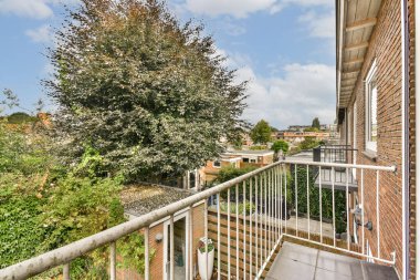 Çağdaş bir balkon manzarası yemyeşil, konut binaları ve berrak mavi gökyüzü huzurlu bir şehir ortamı yaratıyor..