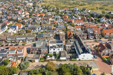 Panoramik bir hava manzarası, çeşitli ev stilleri, çatılar ve doğal ortamda yerleşmiş peyzaj alanlarıyla dolu canlı bir yerleşim yeri gösteriyor..