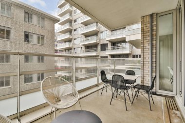 Modern mimari ve şehir yaşamının sergilendiği şık bir balkon, cam parmaklıklar ve berrak bir gökyüzü altında minimalist mobilyalar..