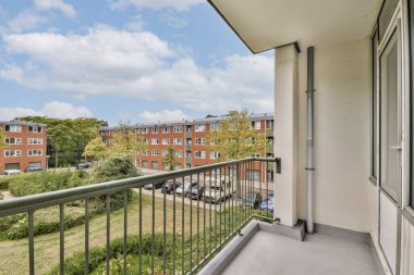 Geniş bir balkon yeşil ve mavi gökyüzü ile canlı bir yerleşim alanına bakıyor. Rahatlamak ve dışarıda eğlenmek için mükemmel..