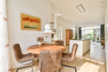 Ahşap bir masa, rahat sandalyeler ve renkli sanat eserlerinin yer aldığı parlak ve davetkar bir yemek alanı, sıcak ve misafirperver bir atmosfer yaratıyor..