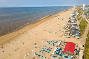 Canlı bir plaj manzarası kumsalda renkli şemsiyeler altında güneşlenir, dalgalar yavaşça kuma vurur..