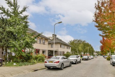 Ağaçlarla ve modern evlerle dolu sakin bir yerleşim yeri manzarası huzurlu bir mahalle atmosferi sergiliyor..
