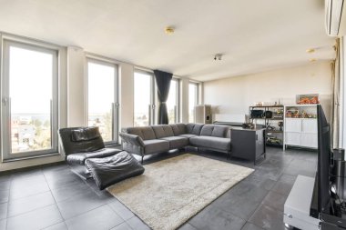 Geniş pencereli şık ve çağdaş bir oturma odası manzaralı, gösterişli mobilyalar ve rahatlamak için mükemmel rahat bir atmosfer sunuyor..