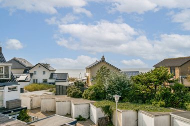 Huzurlu bir denizin ve bulutlu bir gökyüzünün arkaplanına karşı zarif evlerin yer aldığı pitoresk bir kıyı manzarası. Doğa ve mimarinin mükemmel bir karışımı..