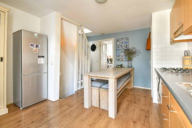 Modern bir buzdolabı, ahşap yemek masası ve havadar atmosferi güçlendiren parlak duvarlar içeren iyi tasarlanmış bir mutfak. Aile yemekleri için ideal..