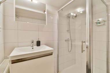 Gösterişli, modern bir banyo düzeneği minimalist lavabo ve çağdaş aksesuarların yanında bir duş kabini sergiliyor, temizliği ve stili vurguluyor..