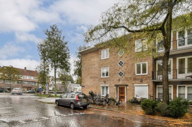 Modern binalar, yeşillikler ve ıslak kaldırımlarla dolu bir yerleşim bölgesini gösteren manzaralı bir görüntü yağmurdan sonra sakin bir atmosferi yansıtıyor..