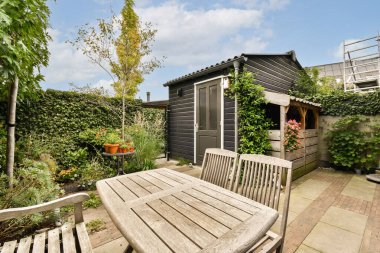 Sade bir bahçe sahnesi, kırsal bir kulübe, zarif bitkiler ve ahşap mobilyalardan oluşan büyüleyici bir açık hava koltuğu, rahatlama ve toplanma için mükemmel..