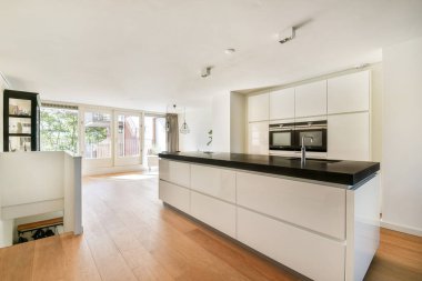 Parlak, modern bir mutfak, açık renkli dolaplar ve geniş pencerelerden yayılan doğal ışıkla aydınlatılmış geniş bir tasarım..