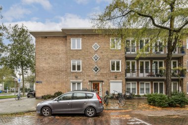 Etrafı yeşilliklerle çevrili ve bulutlu bir gökyüzüne karşı kurulmuş, şık, modern bir apartman..