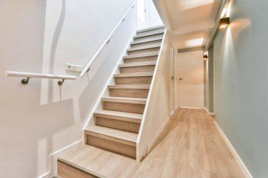 Şık bir merdiven, ahşap basamaklar ve davet edici bir alana götüren yumuşak ortam aydınlatması içerir. Duvarlar sakinleştirici renklerle boyanır, dingin bir atmosfer yaratır..