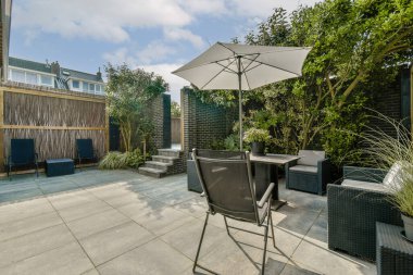Rahat bir oturma, bereketli yeşillik ve rahatlama ve toplanma için mükemmel şık bir şemsiye içeren huzurlu bir bahçe alanı..