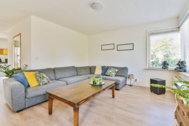 Güneşli bir günde pencerenin önünde kanepesi ve sehpası olan bir oturma odası bahçeye bakıyor.