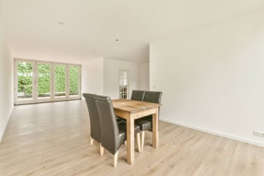 Boş bir odada bir tahta masa ve siyah sandalyeler.