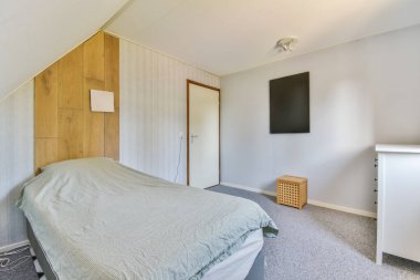 Duvarında televizyon ve önünde yatak olan bir yatak odası. Görüntü bir açıdan çekiliyor.