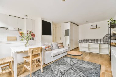 Oturma odası, kanepe, yemek masası ve yatak arasında küçük bir mutfak.