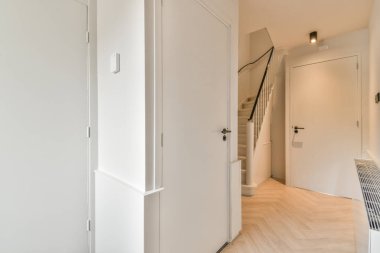 Beyaz ahşap merdivenli beyaz bir koridor üst kata çıkıyor.