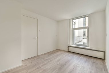 Büyük bir penceresi, ısıtma sistemi ve beyaz duvarları olan boş bir odanın içinde.