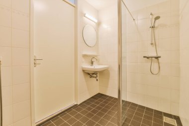 Modern banyoda aynalı lavabo ve cam kapılı duş kutusu ve beyaz fayanslı duvarlar.