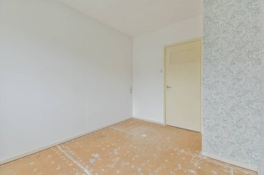 Beyaz kapılı ve duvar kağıtlarının yarısı boş bir oda.