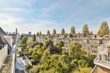 Arka planda ağaçlar ve binalar olan bir apartman dairesi. Balkon penceresinden şehre doğru çekilmiş.