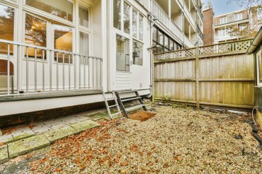 Çitin yanında yaprakları olan bir arka bahçe ve arka planda bazı ağaçlar açık mavi gökyüzü.