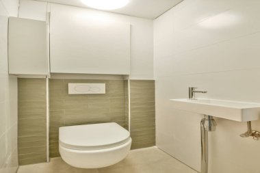 Pürüzsüz ve minimalist bir banyo, temiz hatlar, duvara monte edilmiş bir tuvalet ve küçük bir lavabo. Açık renk paleti geniş görünümü arttırır.
