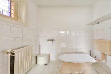 Açık renkli fayansların, modern bir tuvaletin ve şık bir pencerenin olduğu minimalist bir banyo. Mekan aydınlık ve dağınık, basitliği vurguluyor..