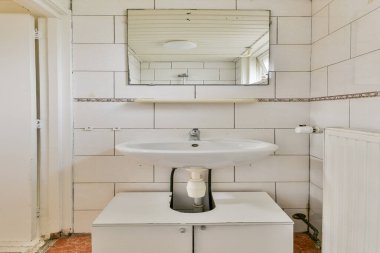 Beyaz bir lavabo, duvara monte edilmiş bir ayna ve minimalist tasarım elementlerinin yer aldığı gösterişli ve çağdaş bir banyo. Mekan iyi aydınlatılmış ve işlevsel..