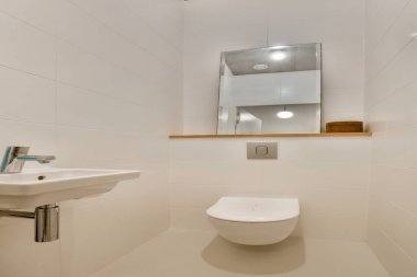 Duvar monte edilmiş tuvalet, minimalist lavabo ve nötr renk düzeni olan şık ve modern bir banyo. Boşluk basitlik ve işlevselliği vurgular.