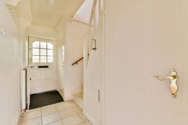 İçinde merdiven, beyaz duvarlar ve ahşap bir kapı olan parlak ve havadar bir modern koridor. Minimalist tasarım basitlik ve işlevselliği vurgular.