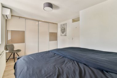 Minimalist mobilyaların olduğu çağdaş bir yatak odası, koyu mavi kapaklı rahat bir yatak ve işlevselliği estetik cazibeyle birleştiren şık bir dekor..