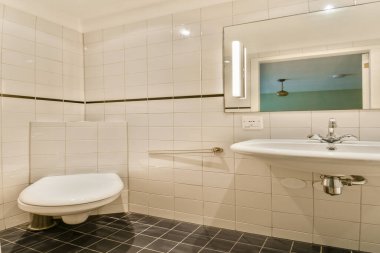 İçinde beyaz seramik fayanslar, parlak bir lavabo ve zarif bir ayna olan çağdaş bir banyo. Tasarım hafif ışıklandırmalı minimalist bir estetiği vurguluyor..
