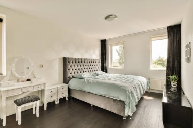 Yumuşak renkleri ve şık mobilyaları olan modern bir yatak odası. Odada bir yatak, bir kibir ve sakin bir atmosfer yaratan büyük pencereler var..