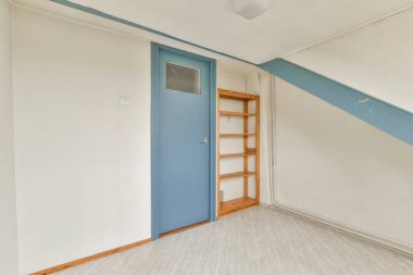 Mavi kapısı ve hafif ahşap rafları olan ferah minimalist bir oda, iç tasarımda basitlik ve işlevselliği vurguluyor.