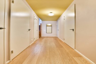 Temiz çizgiler, hafif ahşap döşemeler ve nötr duvarların yer aldığı geniş bir koridor merdiven çıkıyor ve merkezi bir aydınlatma armaşıyla aydınlatılıyor..