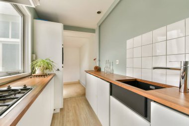 Minimalist dolaplar, ahşap tezgah ve geniş pencerelerden yayılan geniş doğal ışık içeren şık bir modern mutfak..