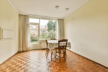 İçinde sandalyeler, büyük pencereler ve minimalist dekorların bulunduğu iyi ışıklandırılmış bir yemek odası. Toplantılar için mükemmel bir ortam yaratıyor..