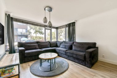 Havalı, koyu renkli bir kanepe, yuvarlak bir sehpa ve geniş pencereli oturma odası, doğal ışığın boşluğu doldurmasına olanak sağlıyor..