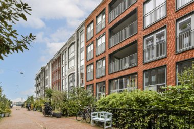 Parlak bir gökyüzü altında şık daireler ve bisiklet dostu yollar bulunan, yeşillikle kaplı modern bir yerleşim bölgesini gösteren manzaralı bir manzara.