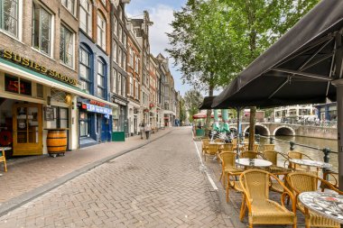 Geleneksel binalarla ve bir kanalın yanında, Amsterdam mimarisinin canlı atmosferini gözler önüne seren manzaralı bir cadde..