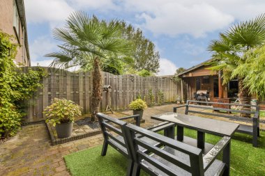 Canlı yeşillikler, palmiye ağaçları ve yemyeşil çimlere kurulmuş rahat bahçe mobilyalarının yer aldığı davetkar bir bahçe sahnesi, rahatlama ve açık havada toplanma için mükemmel..