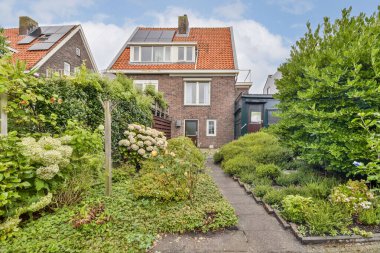 Bu resim, çeşitli bitkiler, çiçekler ve iyi korunmuş yeşilliklerle dolu canlı bir bahçeyle çevrili büyüleyici bir evi gözler önüne seriyor..