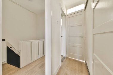 Beyaz duvarlar ve ahşap döşemeler de dahil olmak üzere modern tasarım elementlerinin yer ve ışık hissini geliştirdiği parlak ve havadar bir koridor..