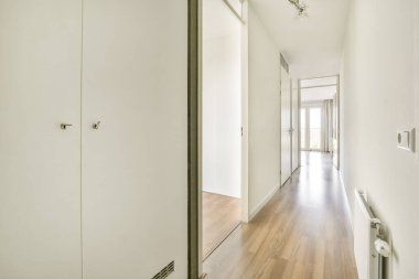 Odalara açılan, ahşap döşeme ve beyaz duvarlı minimalist tasarımı olan modern bir iç mekan koridoru..