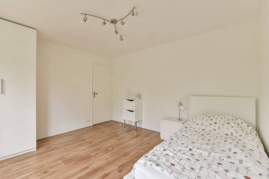 Beyaz duvarlar, ahşap döşemeler ve basit dekorasyon unsurları olan temiz ve minimalist bir yatak odası. Tasarım, sükunet ve basitlik duygusunu teşvik ediyor..